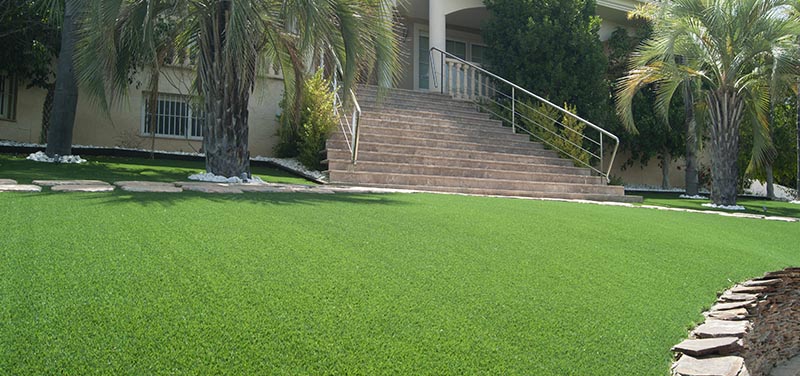 Jardín de césped artificial con escaleras y vegetación